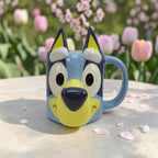 Taza 3D de cerámica Magia Nostálgica con forma de la cara de Bluey en tonos azules y amarillos sobre mesa de jardín
